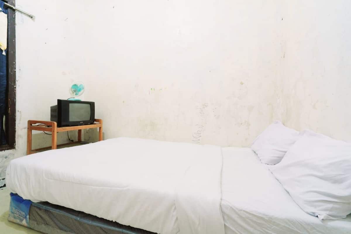 A small, simple room with a bed, a wooden nightstand, and a television.