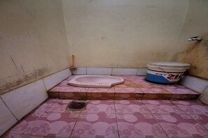 A small, tiled bathroom with a toilet, a bucket, and a drain. - Hotel O Siliwangi Guest House Syariah (Bandung)