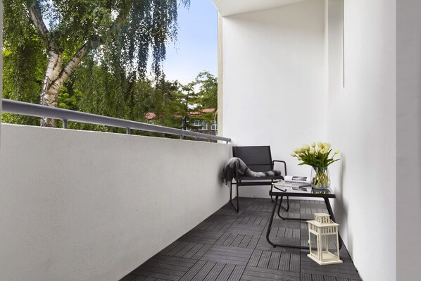 A balcony with a black chair, a small table with a vase of flowers, and a white lantern. - Elite Apartments Chicky Deluxe (Gdansk)