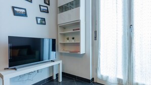 A modern living room with a flat-screen TV on a white stand, a white cabinet with shelves, and a large window with curtains. - Sui tetti di Torino by Wonderful Italy (Torino)