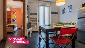 A modern kitchen with a dining table, chairs, and a refrigerator. There is a window with curtains, a television on a stand, and a shelf with decorative items. - Sui tetti di Torino by Wonderful Italy (Torino)