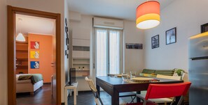 A modern kitchen with a dining table, chairs, and a refrigerator. There is a window with curtains, a television on a stand, and a shelf with decorative items. - Sui tetti di Torino by Wonderful Italy (Torino)