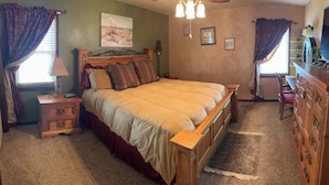 Une chambre à coucher comprenant un lit, des tables de chevet, une commode, un téléviseur et un tableau accroché au mur.