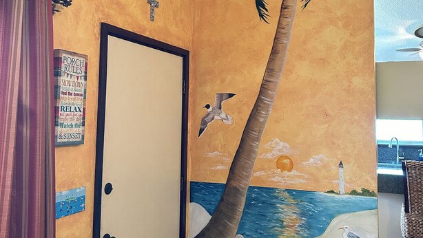 Une pièce décorée d’une fresque représentant une scène de plage, une porte avec une pancarte et un sol à motifs.