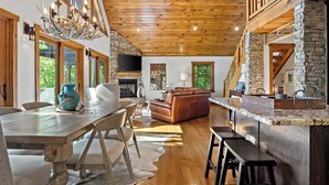 A spacious living area with a wooden ceiling, stone walls, a fireplace, a large sofa, and a dining table with chairs. - Welcome to Grandview Lodge! A 4 bedroom, 4 bath Mountain Sanctuary with Mtn View (Nebo)
