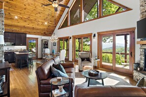 A spacious living area with a high ceiling, wooden beams, a large sofa, a coffee table, and a fireplace.