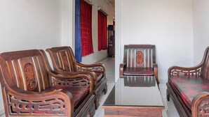 A traditional wooden sofa set with intricate carvings, a glass-top coffee table, and red curtains in a hallway. - Hotel O Guest House Pahlawan Syariah (Kotabumi)