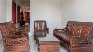 A traditional wooden sofa set with intricate carvings, a matching wooden coffee table, and red curtains in a hallway. - Hotel O Guest House Pahlawan Syariah (Kotabumi)