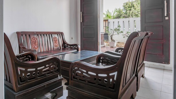 A room with a glass-top table and four wooden chairs with intricate designs. - Hotel O Guest House Pahlawan Syariah (Kotabumi)