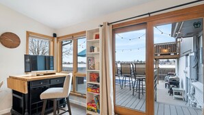A room with a wooden desk, a chair, a bookshelf, and a large sliding glass door leading to an outdoor deck with chairs and a table.