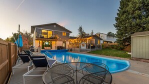 A backyard with a swimming pool, a covered patio area, and a house with a balcony.