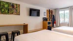 A hotel room with two beds, a TV, a desk with a chair, and a window with curtains.