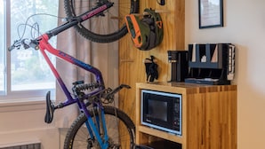 A room with a bed, a wooden wall-mounted bike rack, a microwave, a coffee maker, and a small refrigerator.