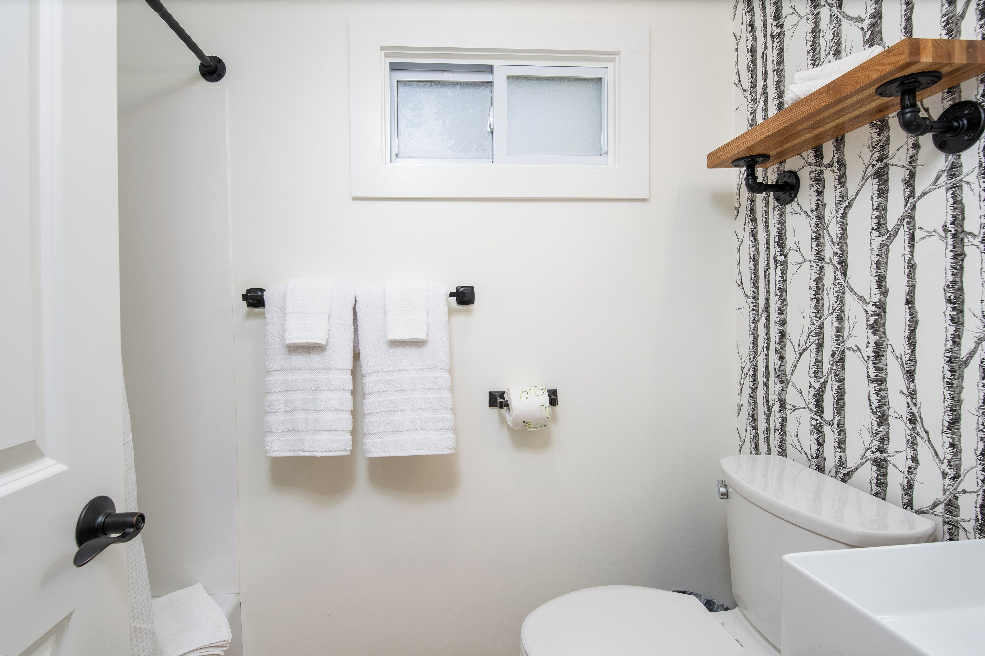 A bathroom with a toilet, a window, a towel rack, and a shower curtain.