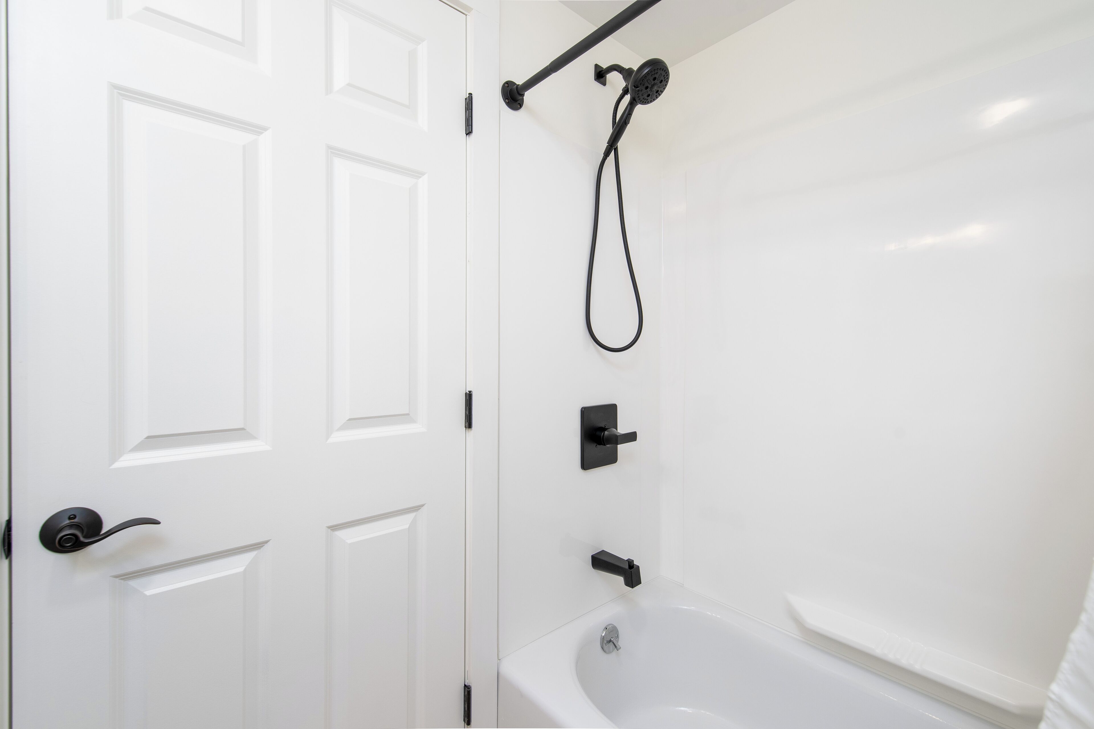 A bathroom with a white bathtub, a showerhead, and a door with a handle.