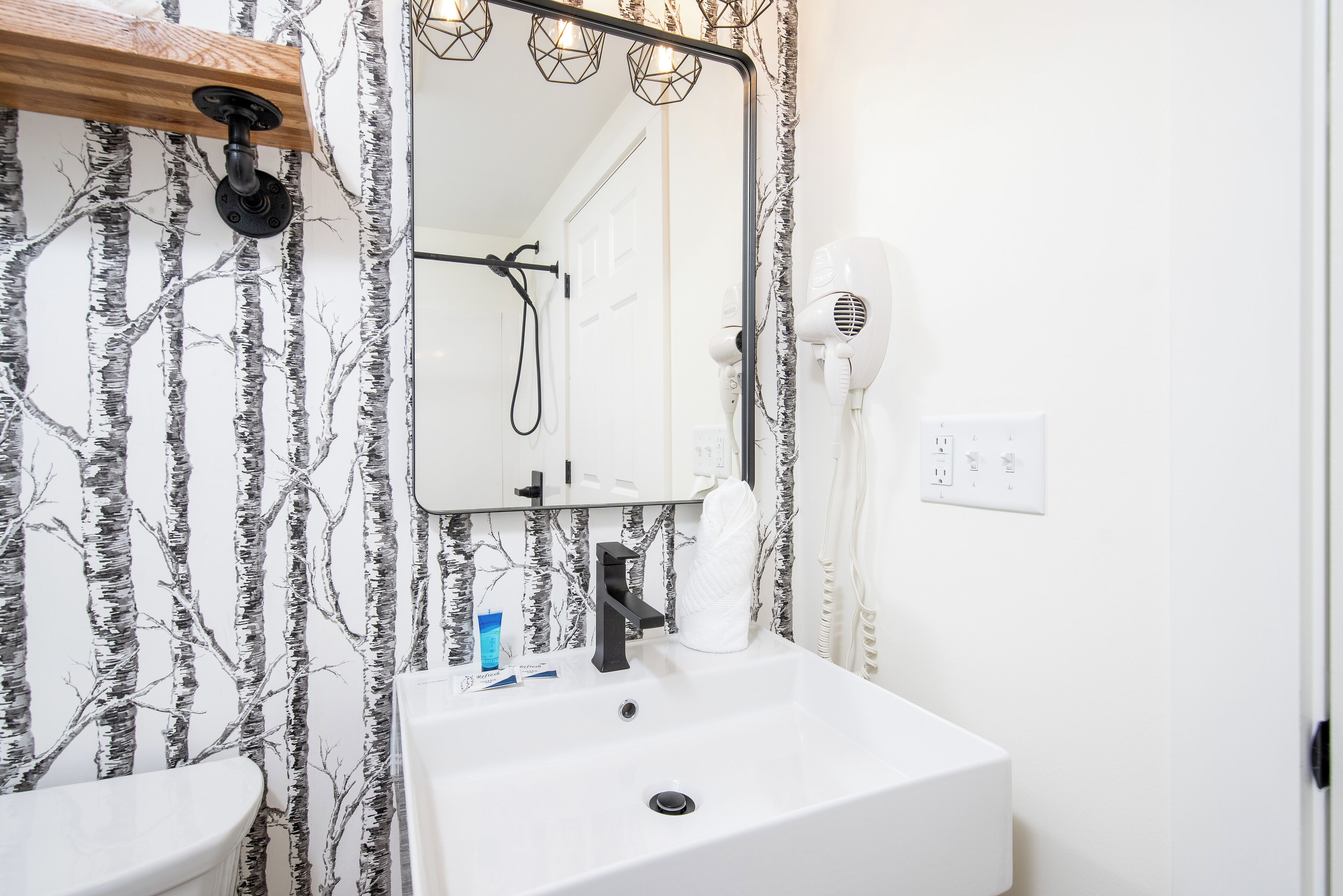 Une salle de bain avec un lavabo blanc, un miroir et un sèche-cheveux.