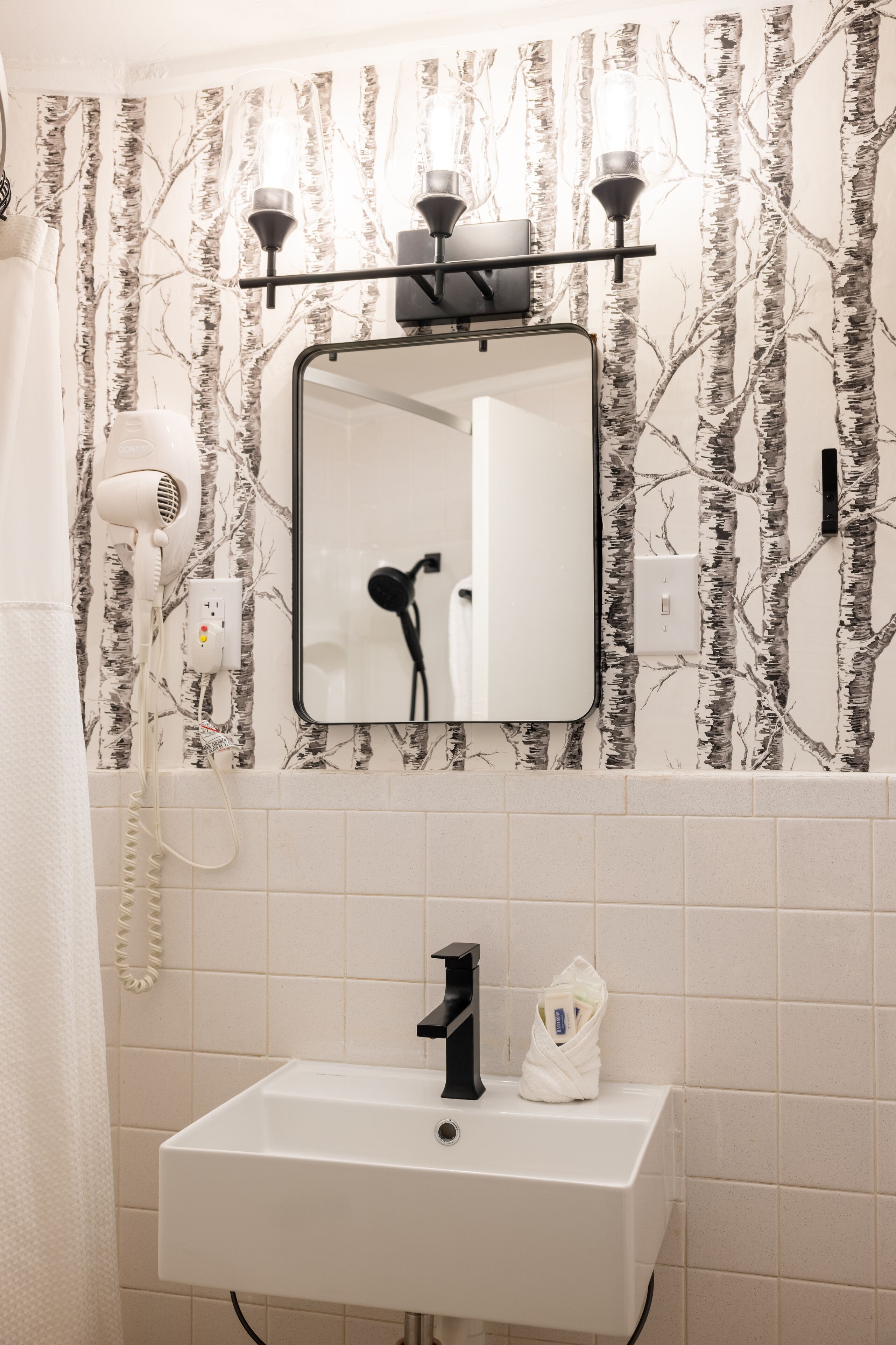Une salle de bain avec un lavabo blanc, un miroir, un sèche-cheveux et un porte-serviettes.