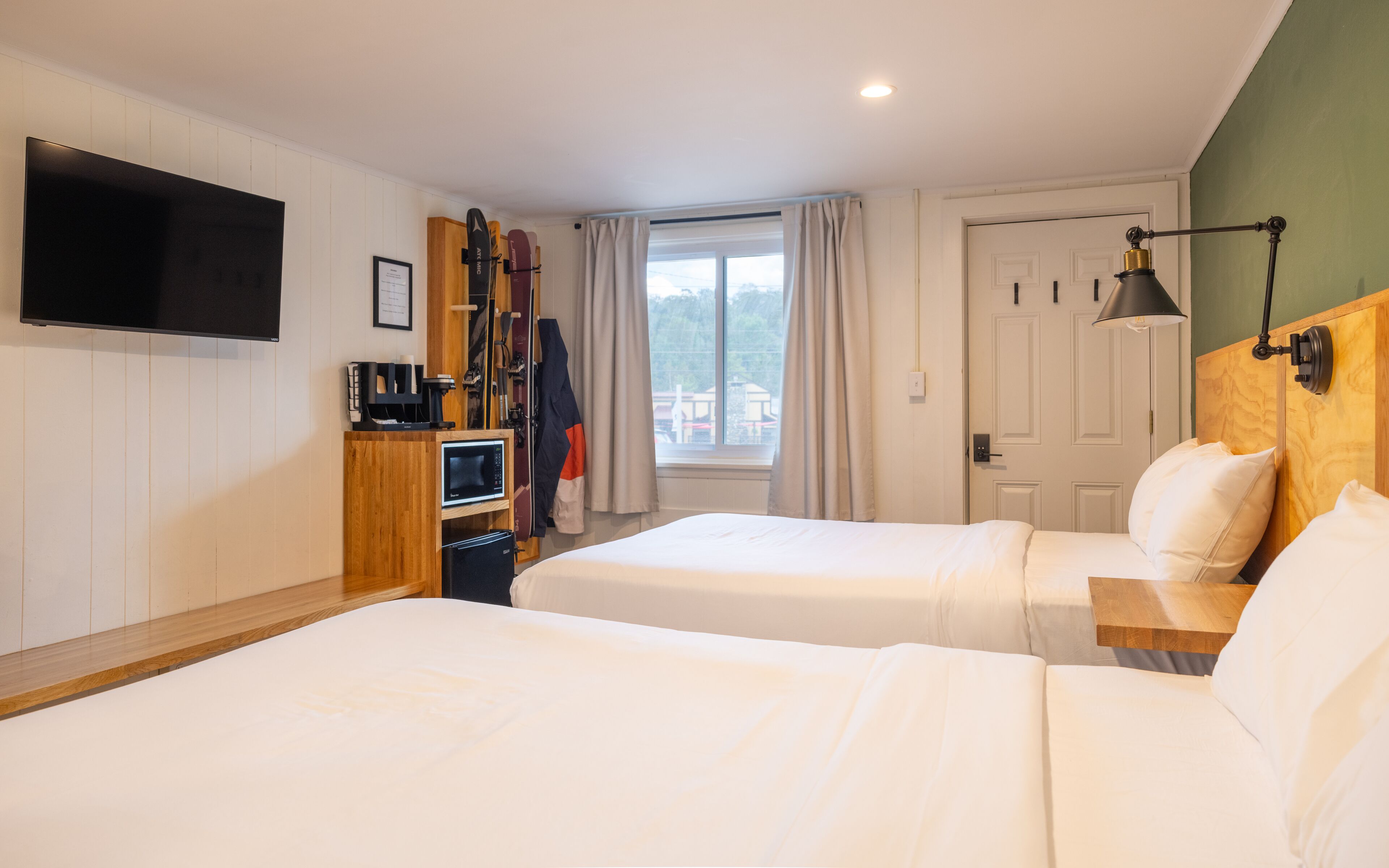 A hotel room with two beds, a TV, a desk, and a window with curtains.