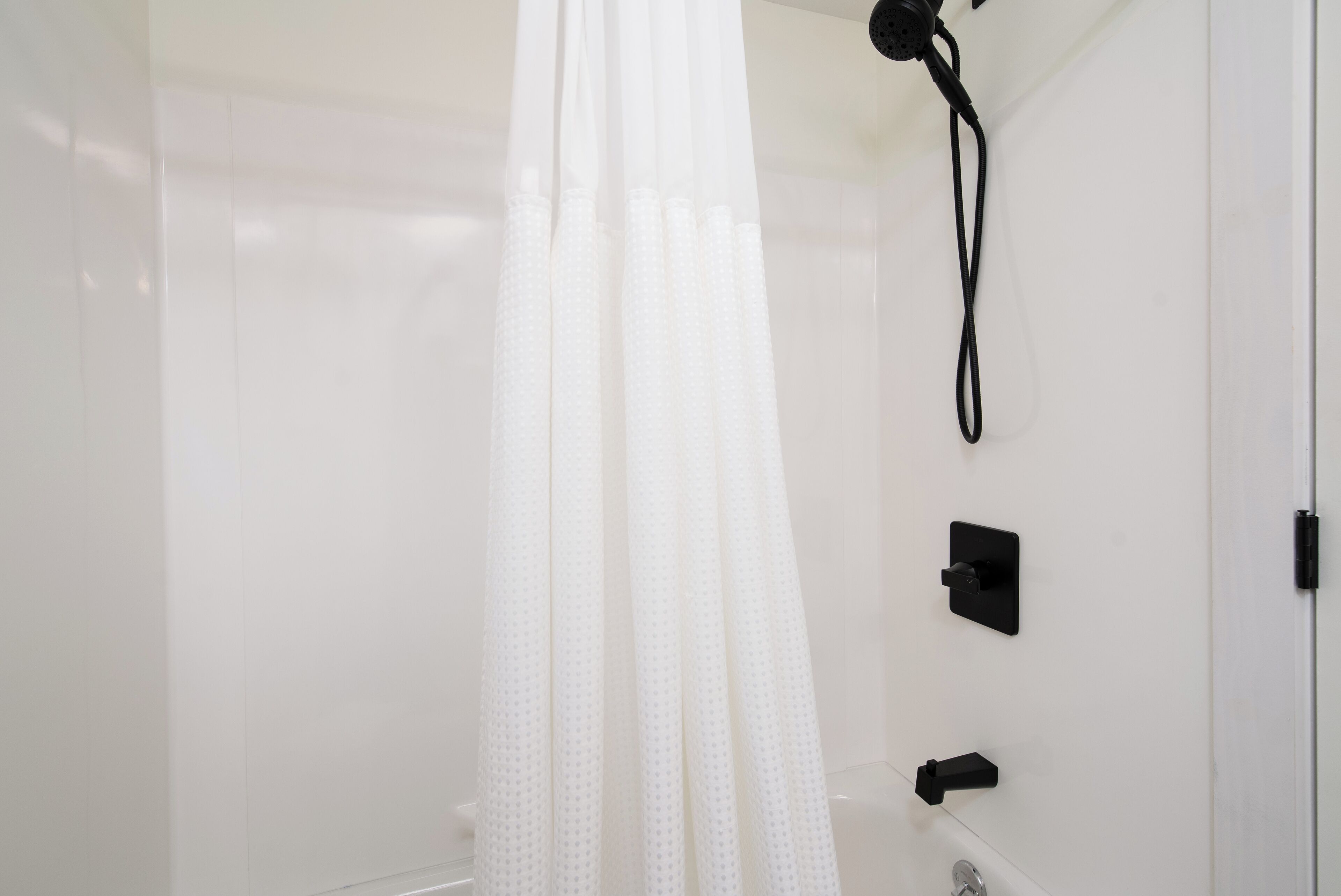 Une salle de bain moderne équipée d’un rideau de douche, d’un pommeau de douche à main et d’un panneau de commande fixé au mur.