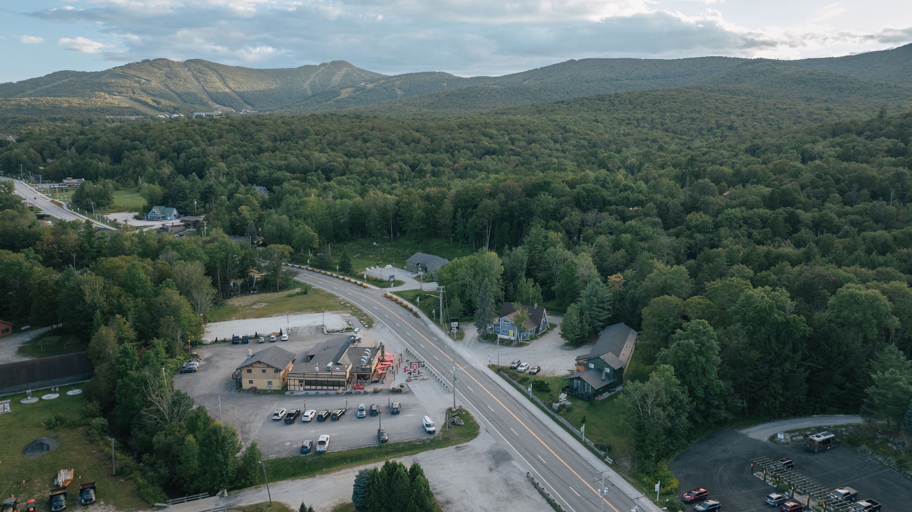 An aerial view of a road leading to a building with a parking lot and a small house nearby.