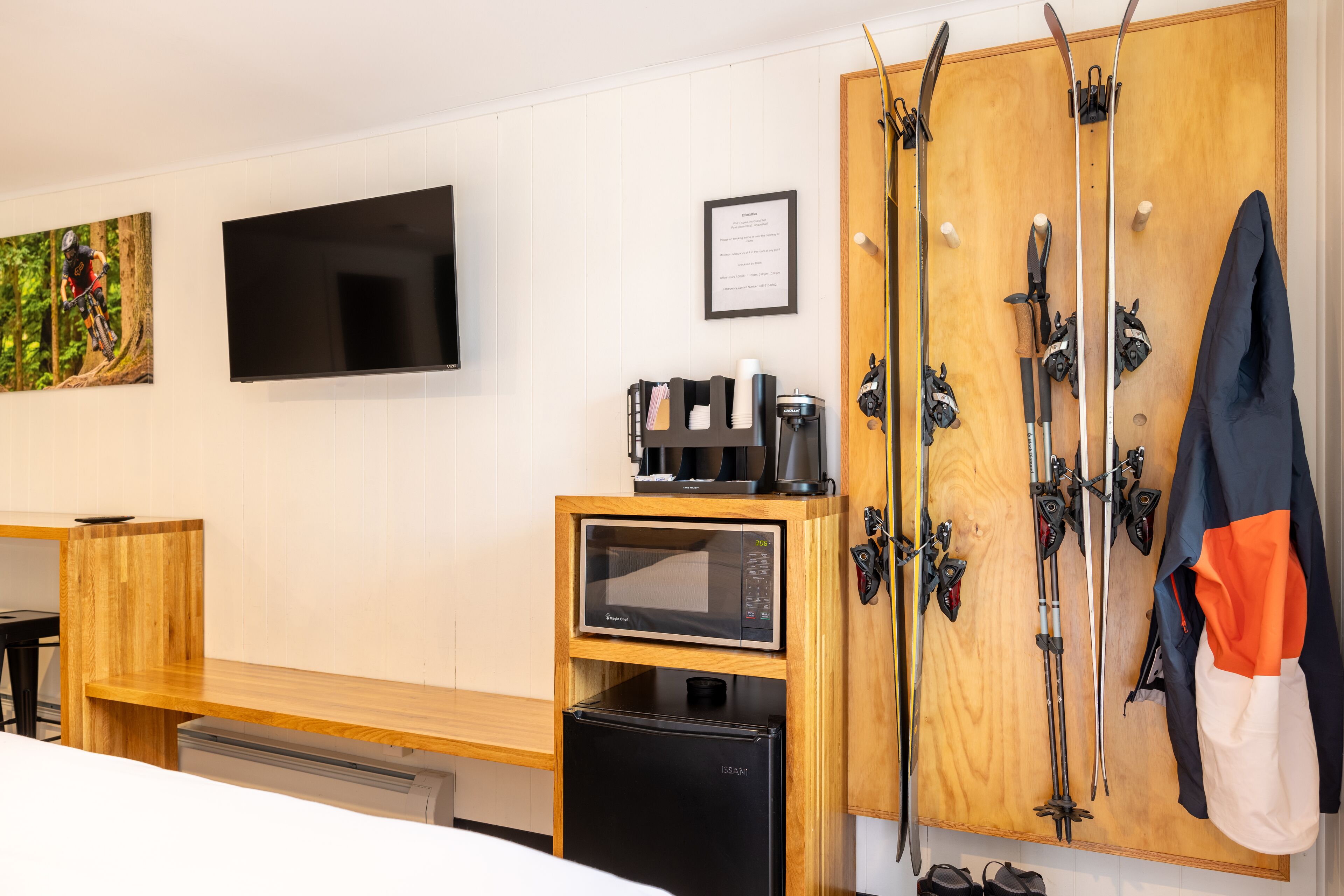 Camera d'albergo con scrivania in legno, microonde, piccolo frigorifero, televisore, sci e appendiabiti.