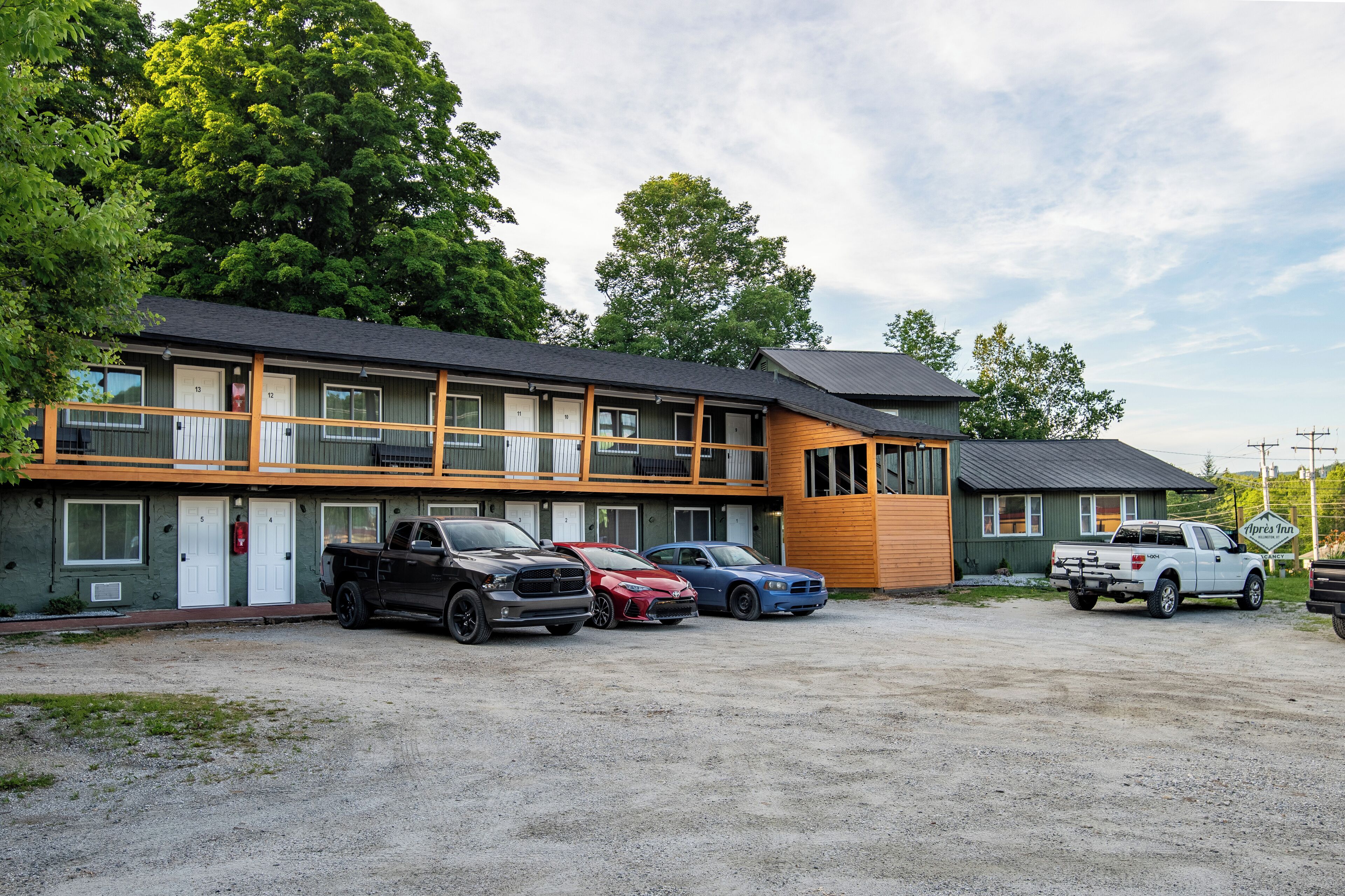A motel with a two-story structure, multiple rooms, and a parking area with several vehicles.