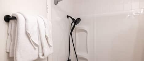 A bathroom with a towel rack holding white towels, a showerhead, and a control panel.