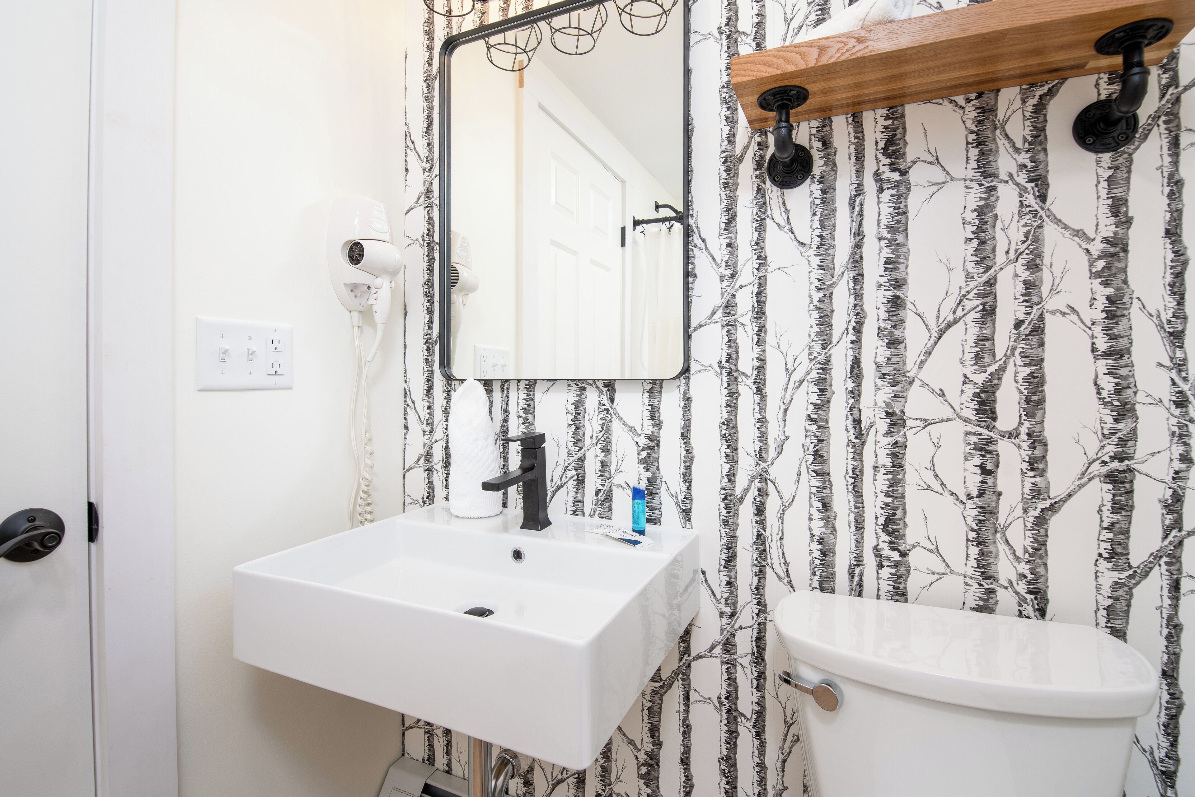 A bathroom with a white sink, a mirror, a toilet, and a wall-mounted hairdryer.