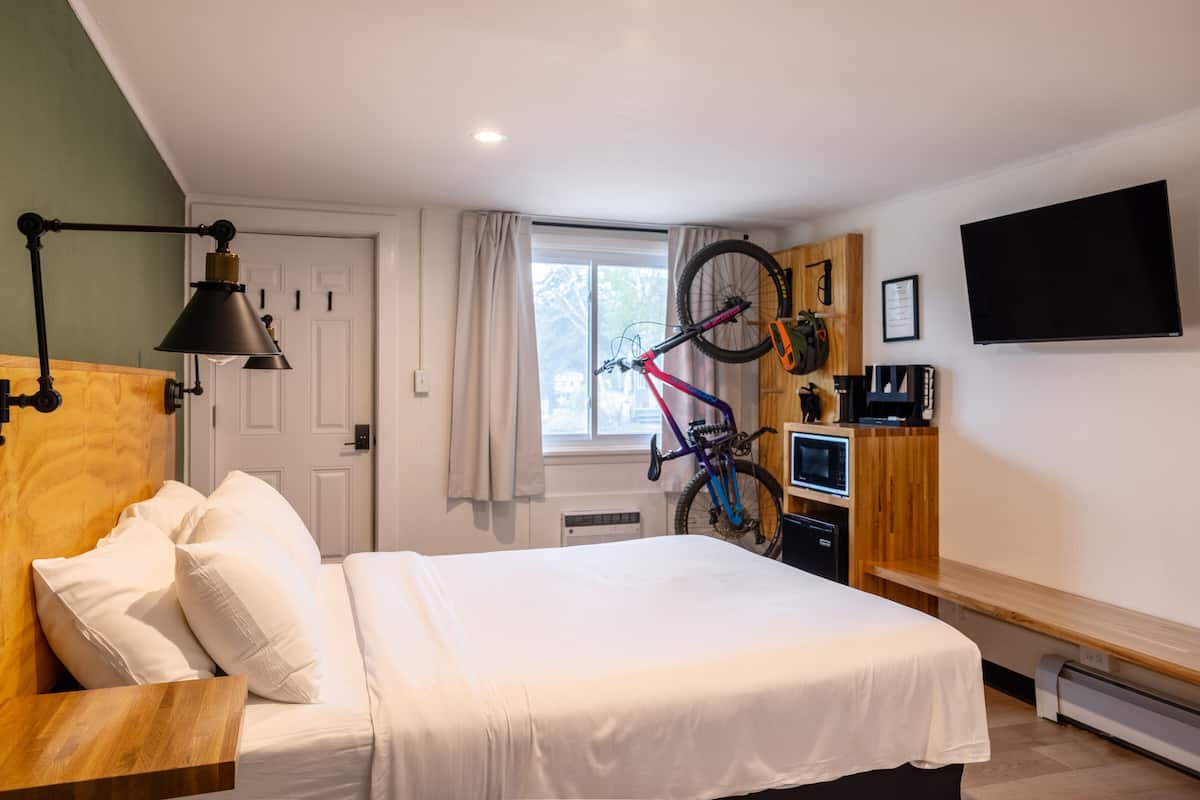 A hotel room with a bed, a desk, a bicycle, a TV, and a window with curtains.