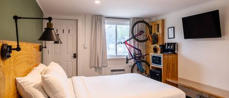 A hotel room with a bed, a desk, a bicycle, a TV, and a window with curtains.