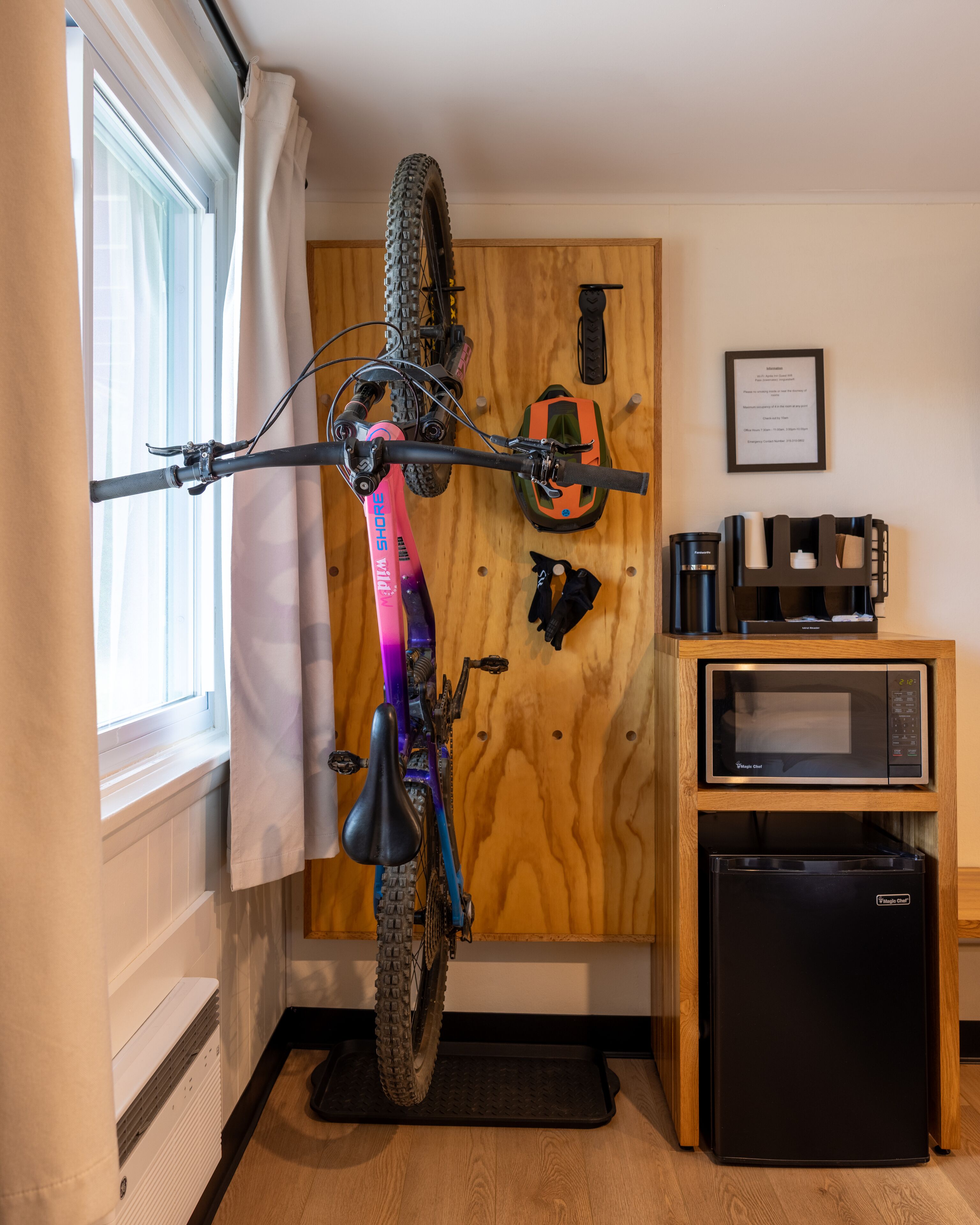 A room with a bicycle mounted on a wall, a microwave, a refrigerator, and a wooden cabinet.