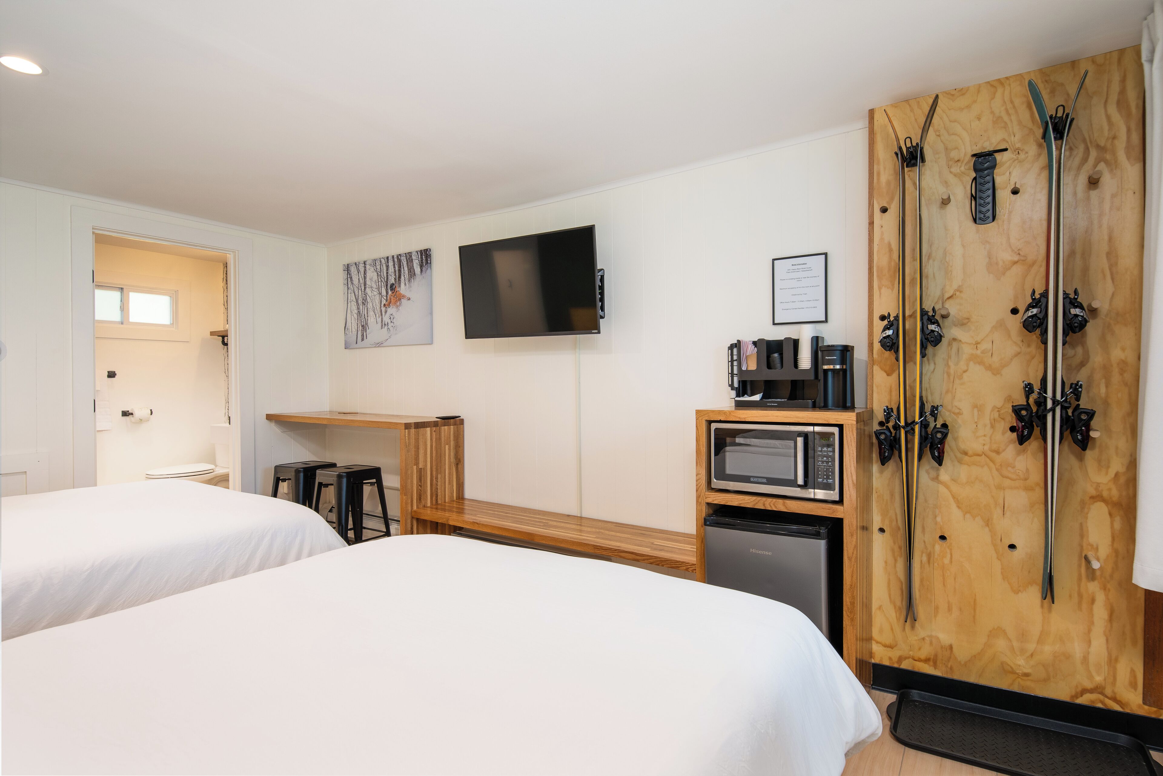 A hotel room with two beds, a TV, a wooden ski rack, a microwave, and a small kitchenette.