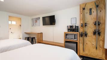 A hotel room with two beds, a TV, a wooden ski rack, a microwave, and a small kitchenette.