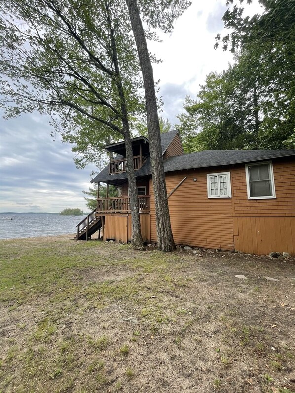 A cabin with a deck and a staircase leading to a second level, located near a body of water.