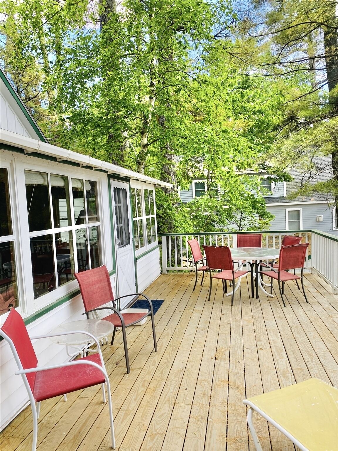 A wooden deck with outdoor seating, a covered area with windows, and a view of a tree-lined street.