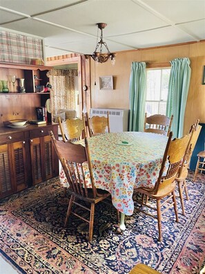 A dining room with a wooden table, chairs, a chandelier, and a patterned rug.
