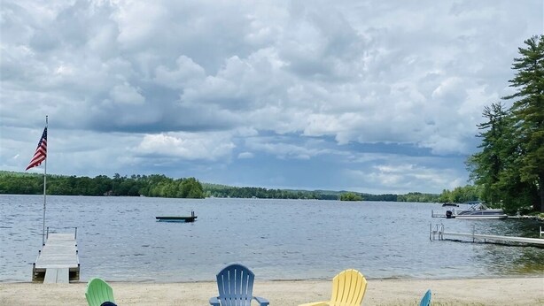 Vista sobre un lago con un muelle, una hilera de sillas Adirondack de colores y una bandera en un asta.