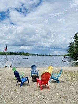 Blick auf einen See mit einem Steg, einer Reihe bunter Adirondack-Stühle und einer Flagge auf einem Mast.