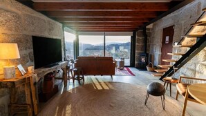 A cozy living room with a stone wall, a fireplace, a television, and a view of the city. - Javardo Family House  (Marco de Canaveses)