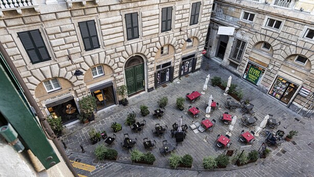 Un patio exterior con suelo de piedra, rodeado de edificios con ventanas y puertas arqueadas.