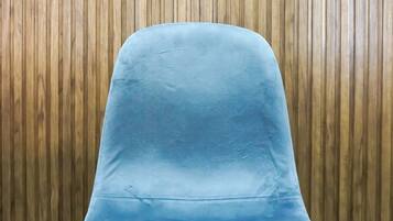 A blue chair with a curved backrest and black legs, positioned against a wooden wall.