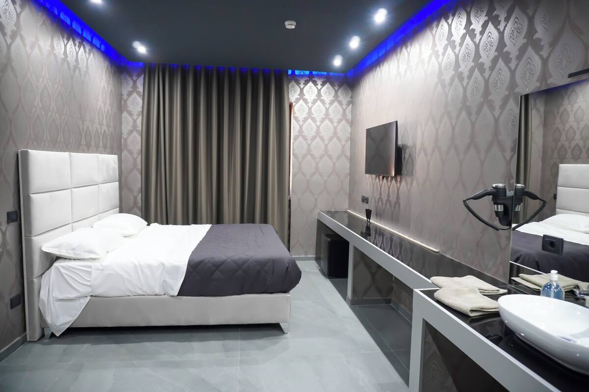 A modern hotel room with a bed, a vanity with a mirror, and a sink.