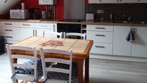 A modern kitchen with white cabinets, a red accent wall, and a dining area with a wooden table and chairs.