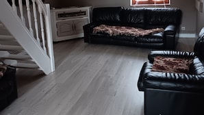 A living room with a wooden floor, a black leather sofa, a white cabinet, and a staircase.