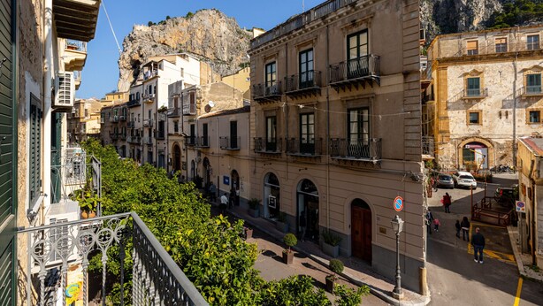 Una calle estrecha bordeada de edificios de varios pisos, balcones y un acantilado rocoso al fondo.