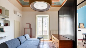 Una sala de estar moderna con un sofá, un aparador de madera y un radiador. Se ve una ventana con vistas a edificios.