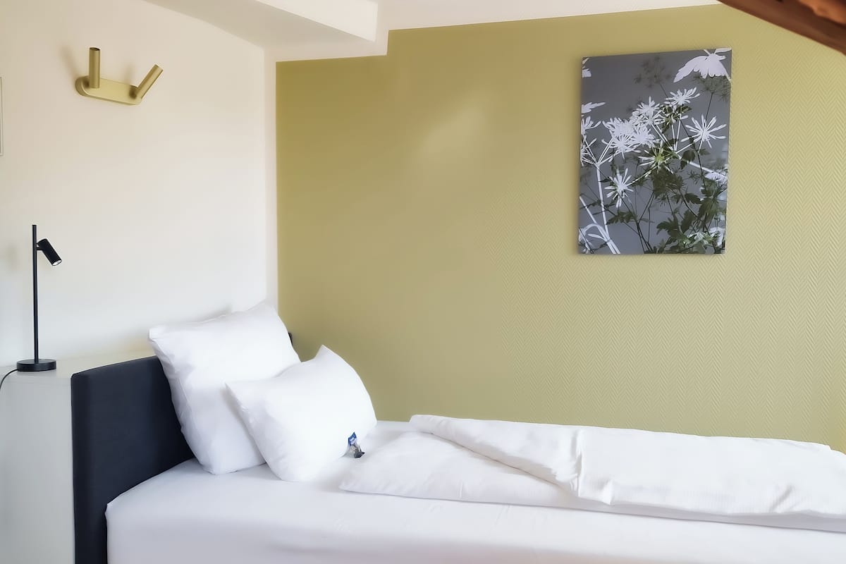 A bedroom with a bed, a nightstand, a wall-mounted light, and a framed picture.