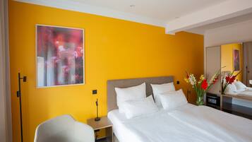 A hotel room with a large bed, a bedside table, a chair, a nightstand, a mirror, and a painting on the wall.