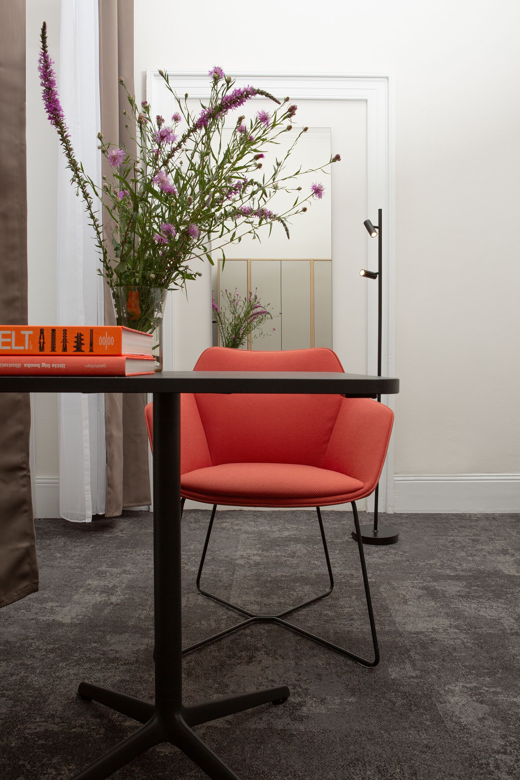 Ein stilvolles Zimmer mit einem roten Sessel, einem Tisch mit Büchern und einer Vase mit Blumen.