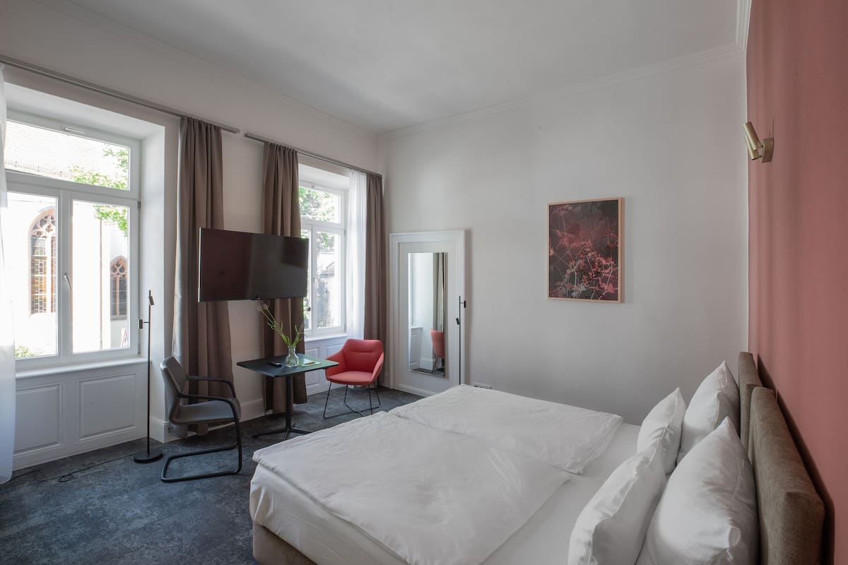 A hotel room with a large bed, a desk with a chair, a television, and a window with curtains.